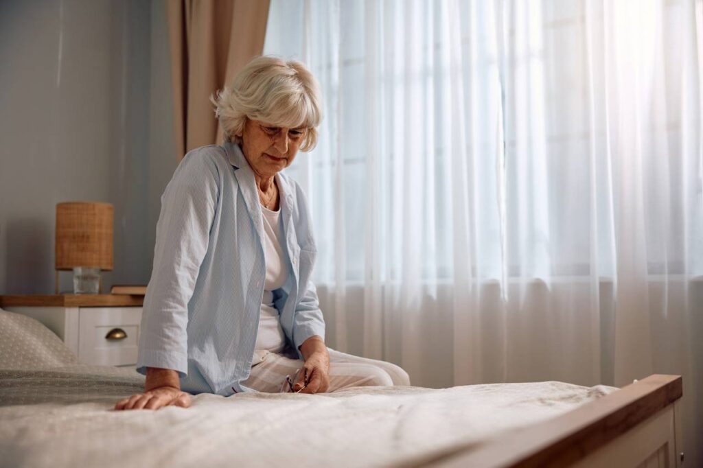 Mulher mais velha sentada na beira da cama